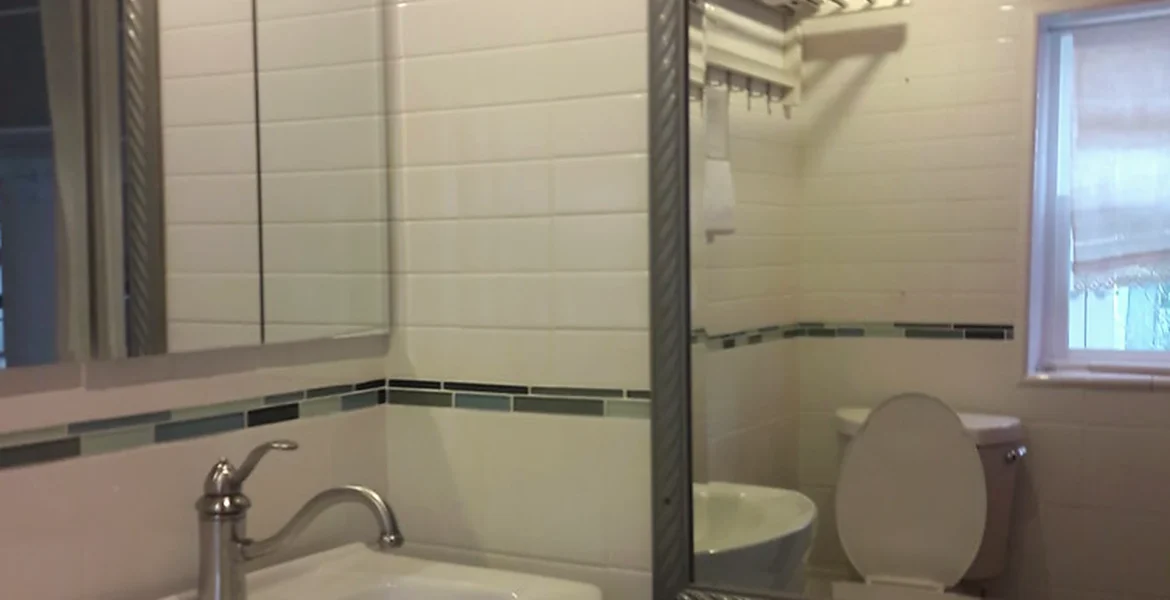 Bathroom wall finishes showing newly tiled walls, basin and fitted mirror