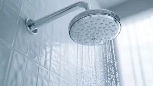 Low water pressure shown by a chrome shower head running a weak flow in a tiled UK bathroom